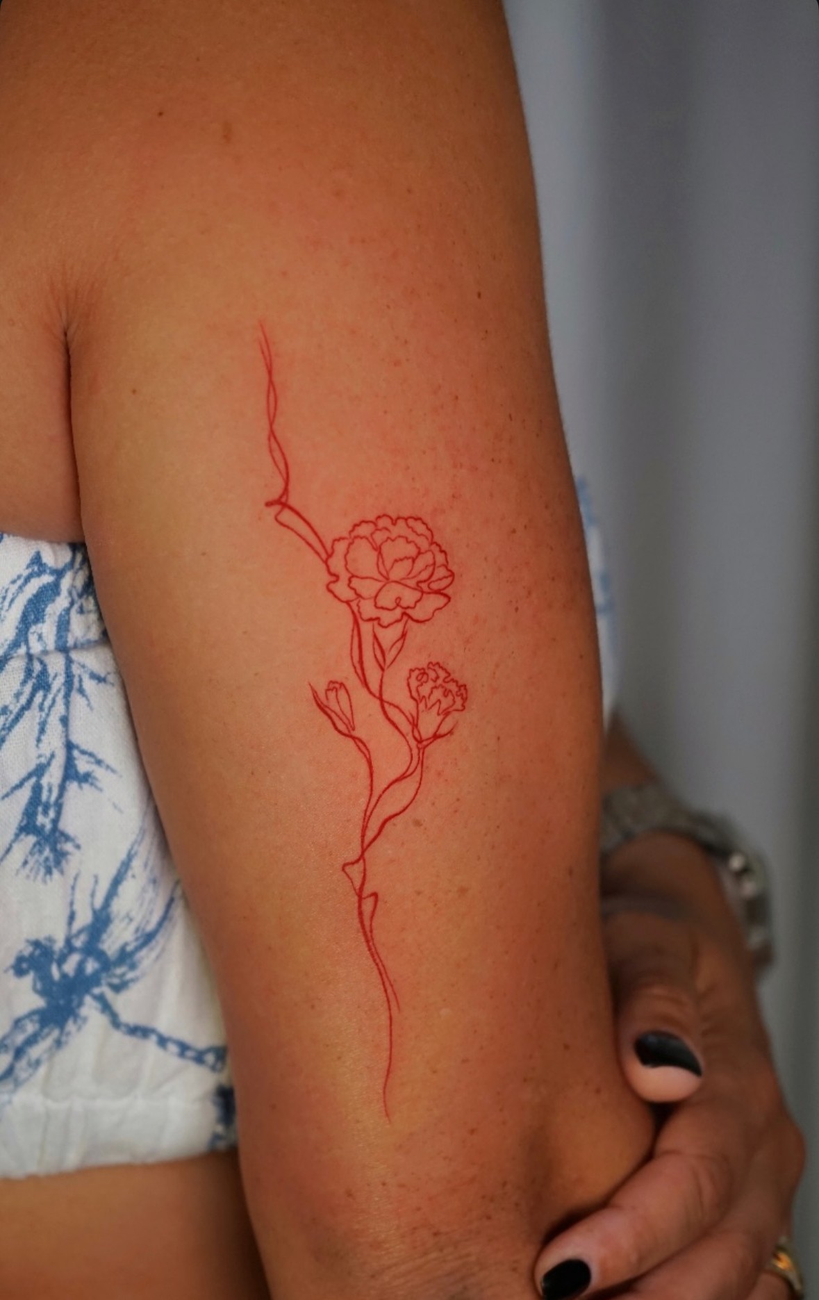 Tatuaje fineline de clavel rojo en el brazo realizado por Shira Tattoo