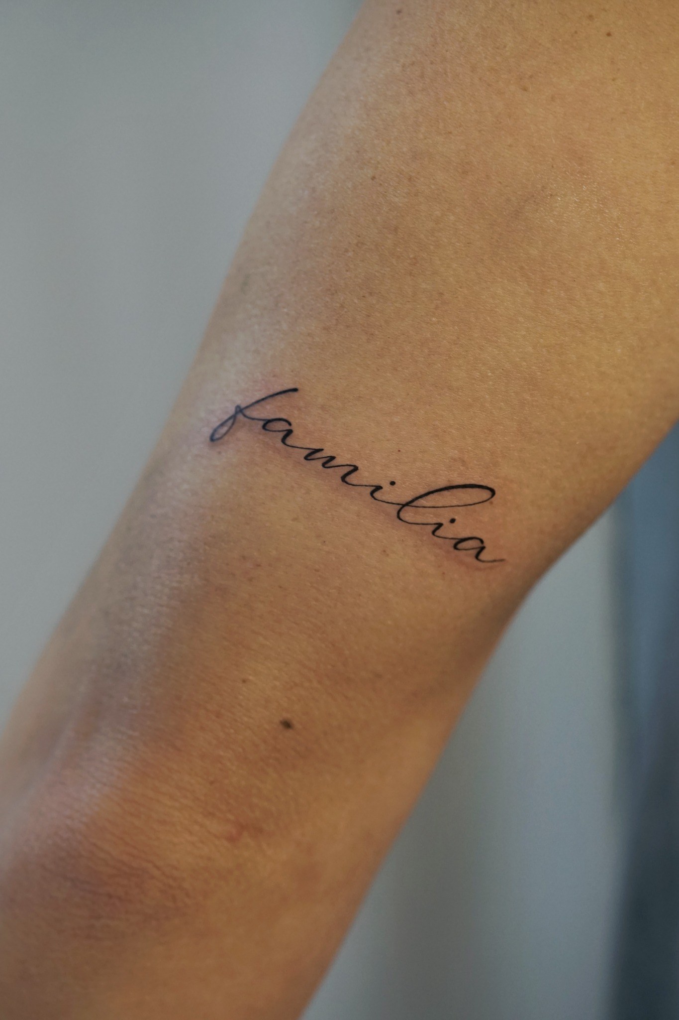 Tatuaje fineline de lettering con la palabra familia realizado por Shira Tattoo