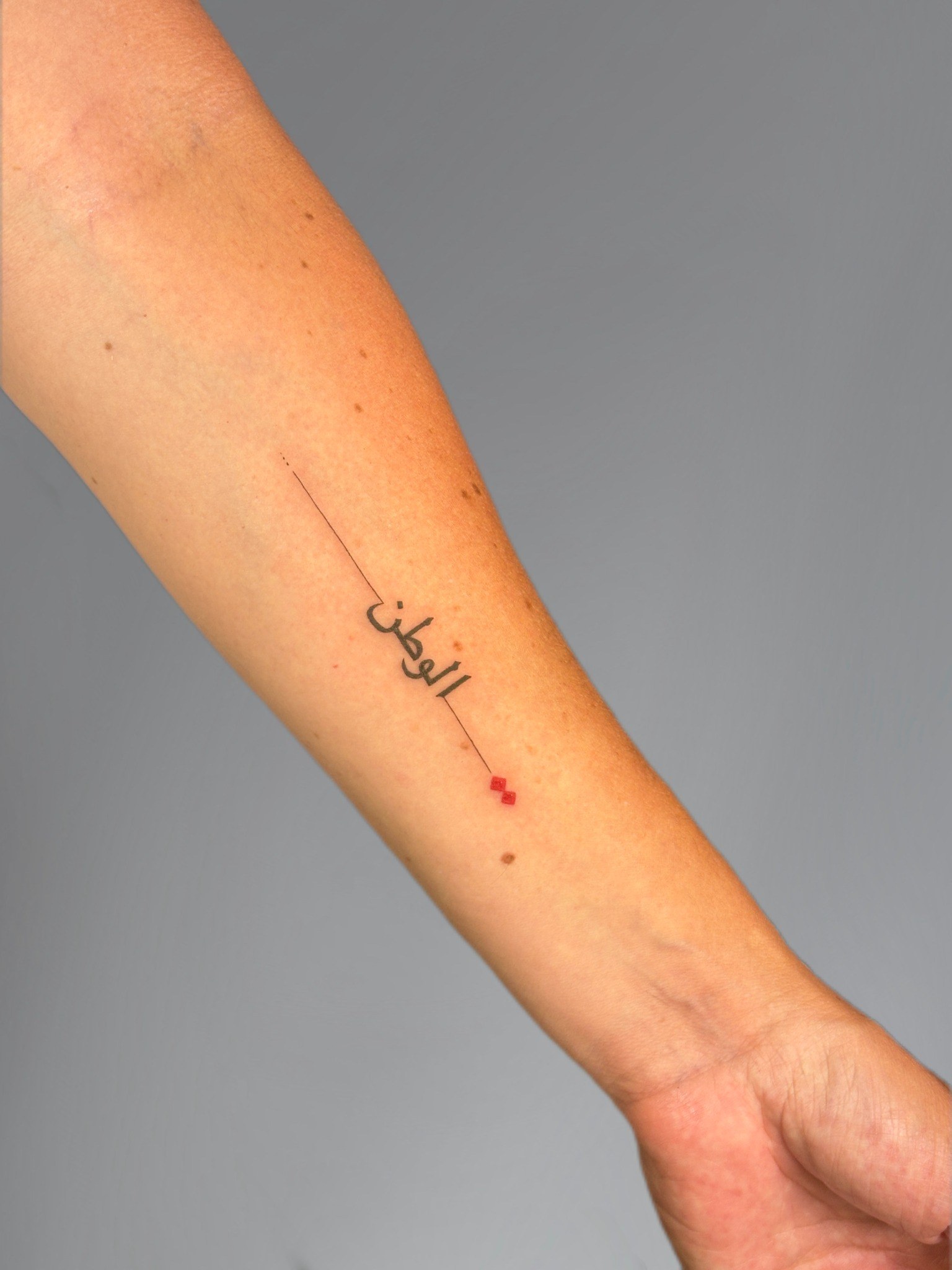 Tatuaje fineline de lettering árabe con detalle rojo realizado por Shira Tattoo