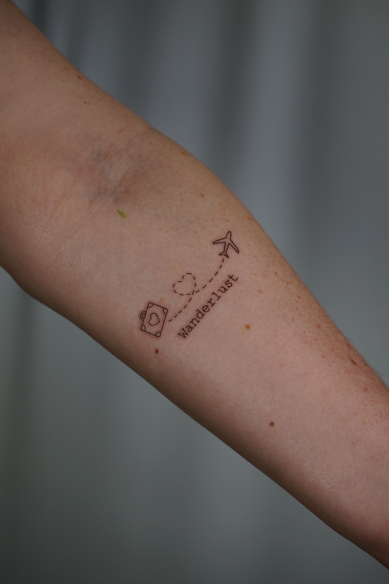 Tatuaje fineline Wanderlust con cámara y avión realizado por Shira Tattoo